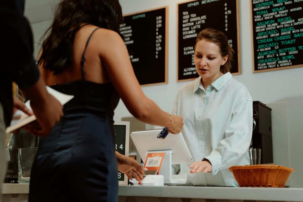 A customer pays with a card at a coffee shop as a barista assists.